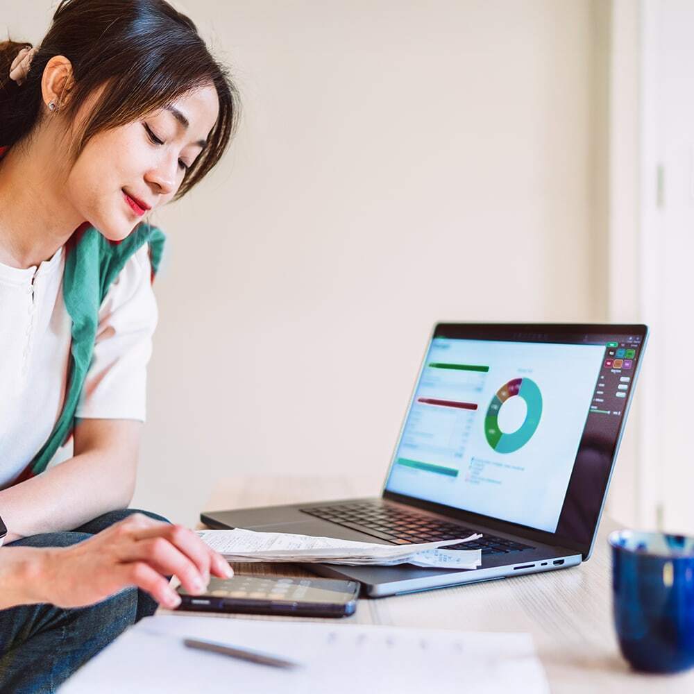 Person using a calculator, with charts displaying data on a laptop to their left