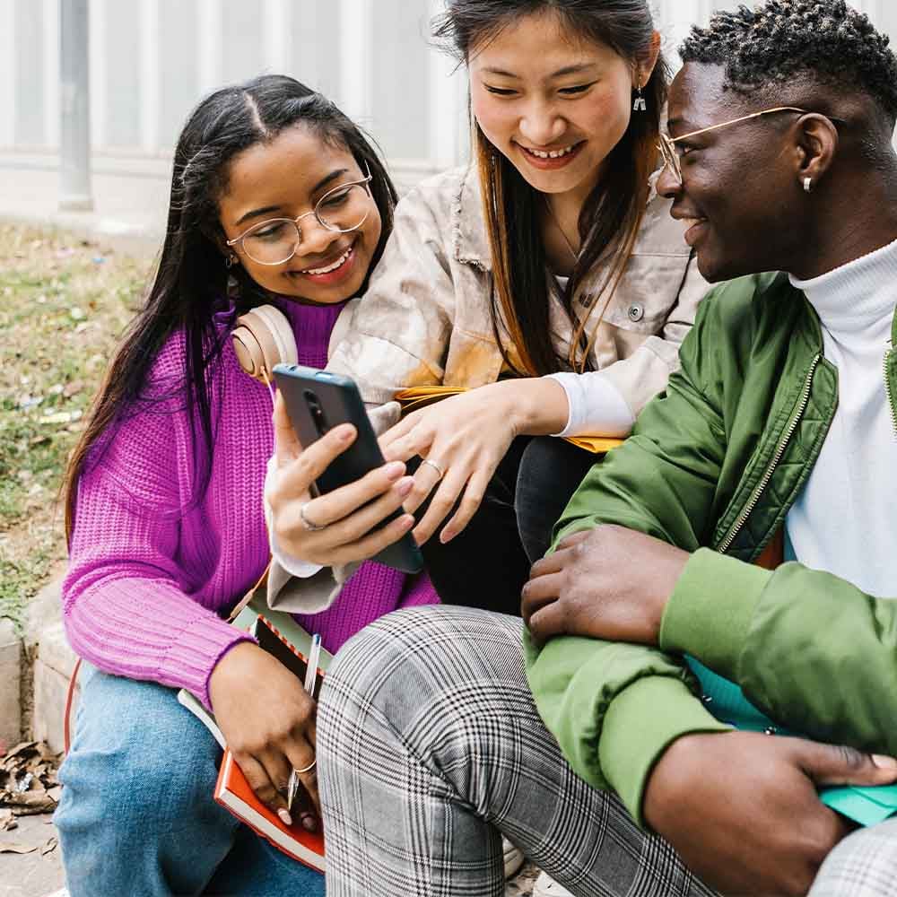 Group of friends gathering around a smartphone and laughing
